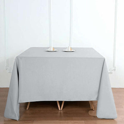 Gray tablecloth draping over a wooden table with candle holders on top.