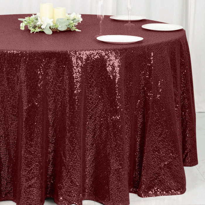 Burgundy sequin tablecloth on a round table with candles and plates.