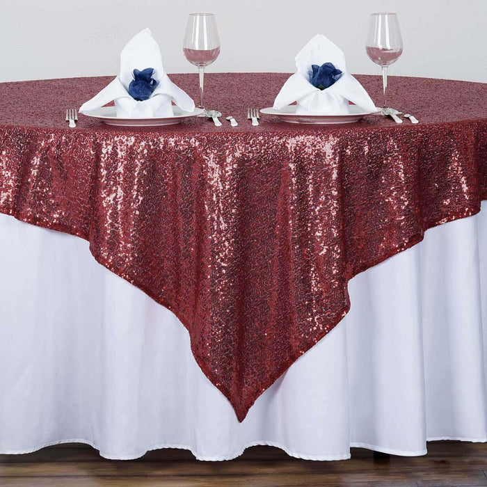 Red sequin tablecloth draping a round table set with elegant napkins and glasses.
