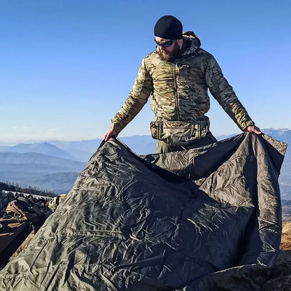 Snugpak Jungle Blanket in olive green being laid on the ground outdoors