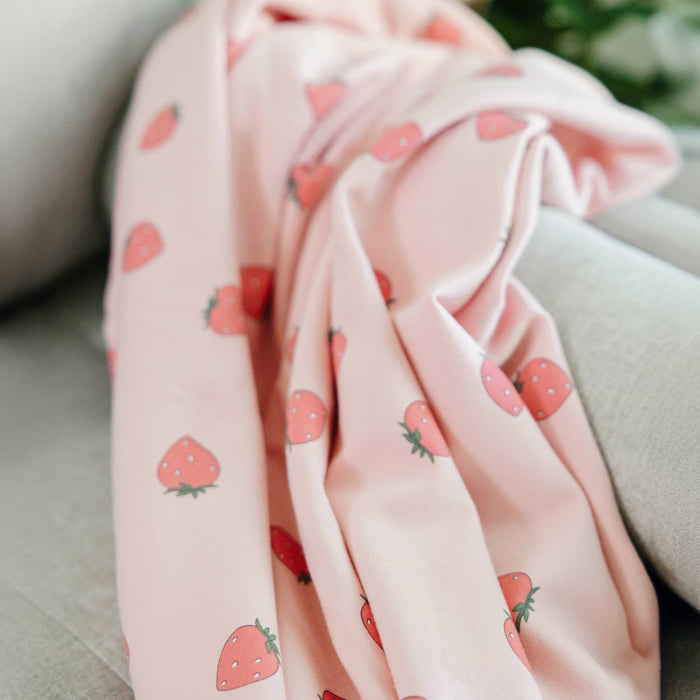 Woolino merino and organic cotton toddler blanket with strawberry pattern draped over a surface